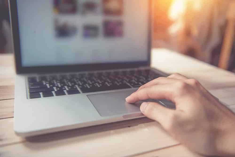 women hand on macbook on wooden table with sun light on background